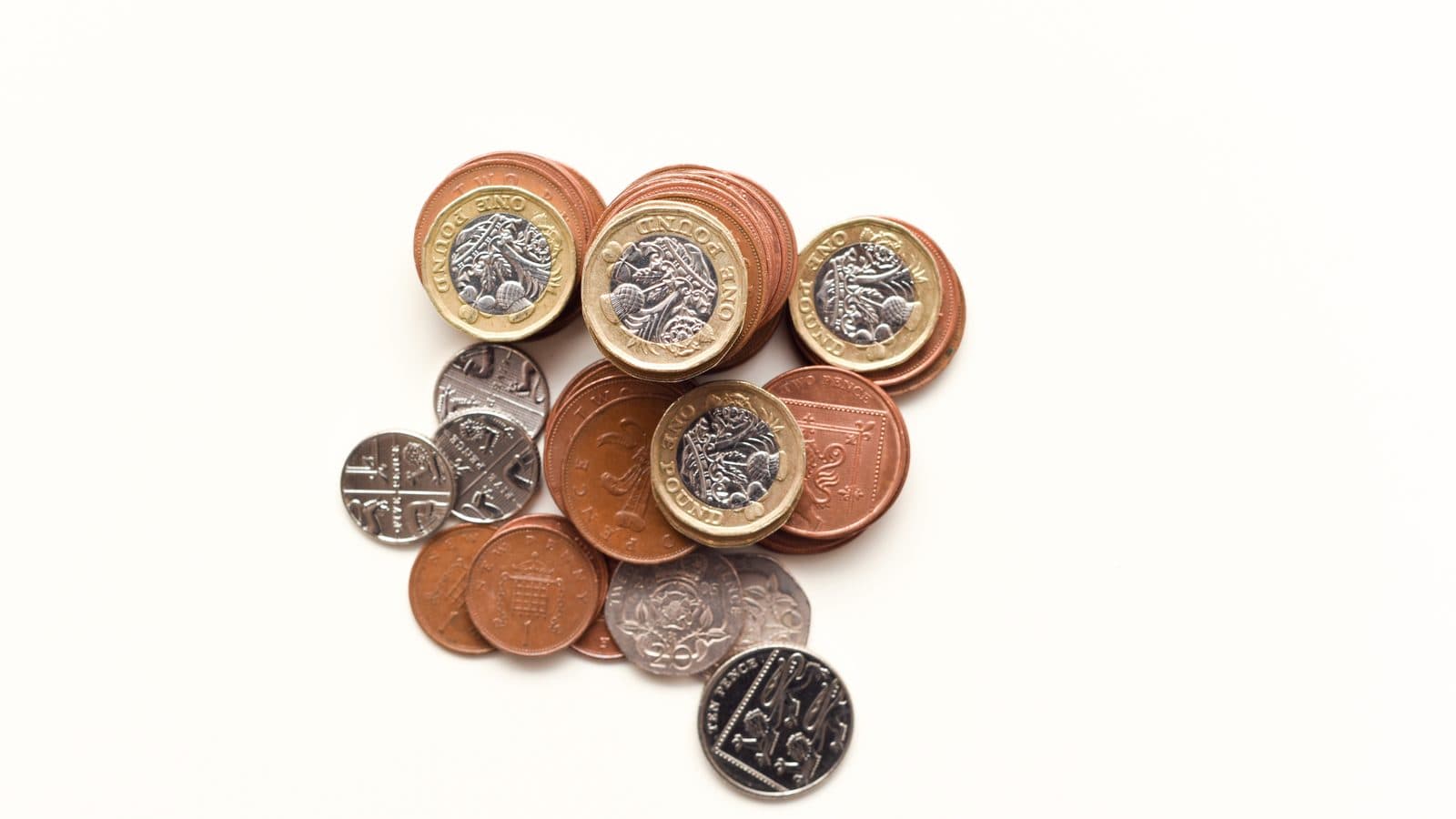A small pile of British pound coins and pennies on a plain white surface