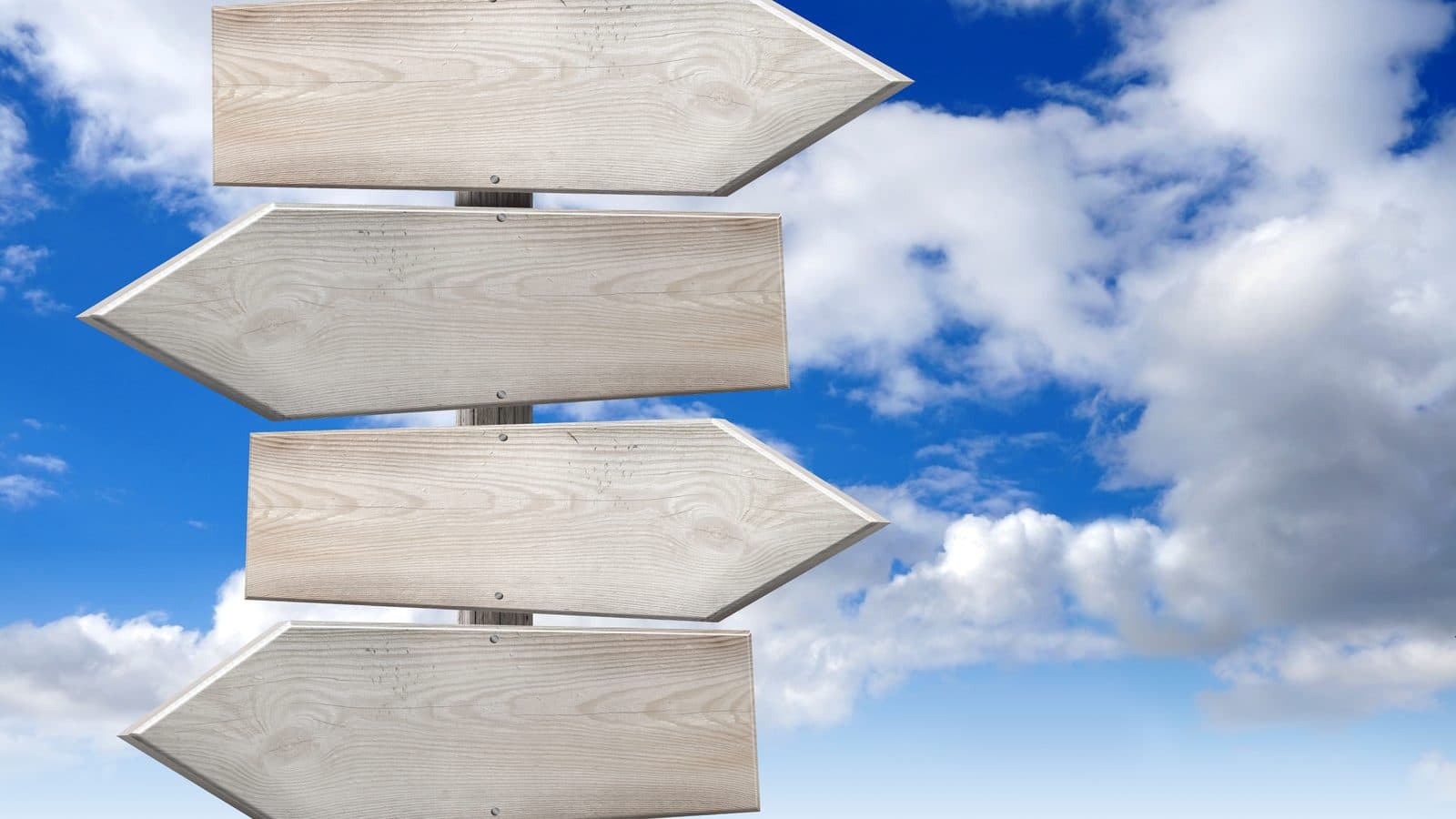 Blank wooden signposts pointing in opposite directions against a blue sky with white clouds